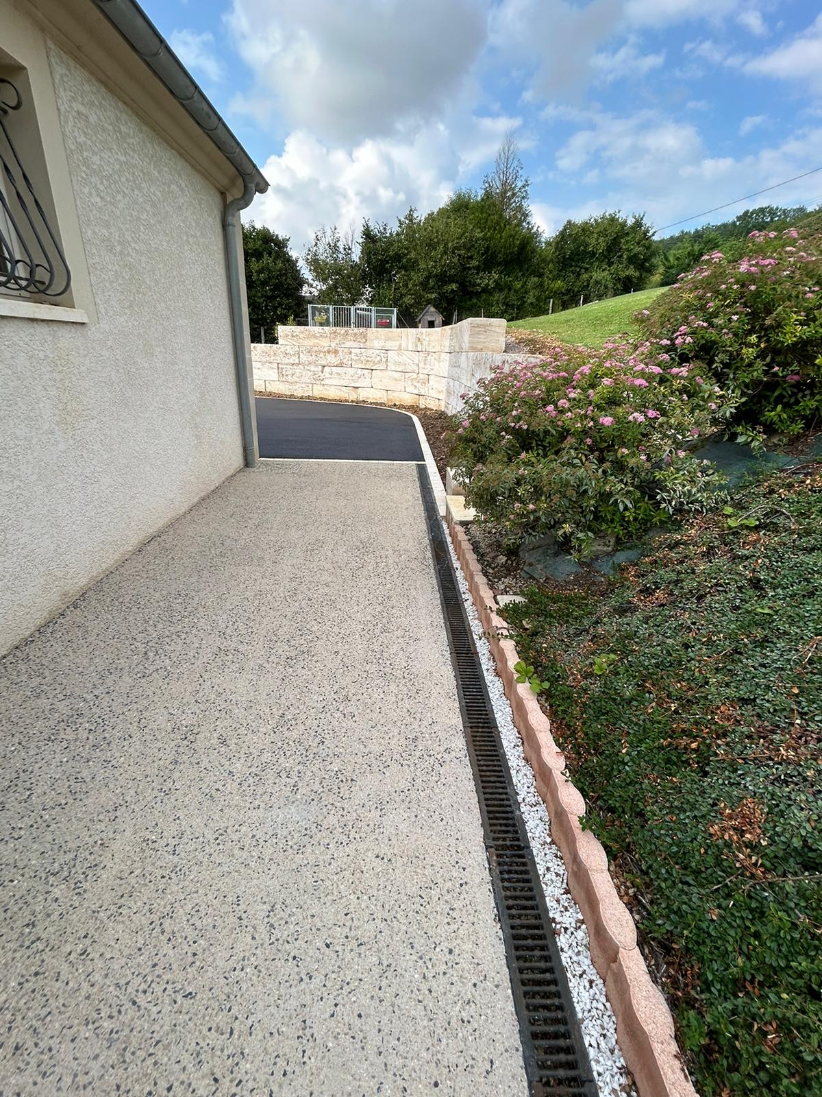 Allée en béton désactivé longée d'un caniveau et d'un muret en pierre